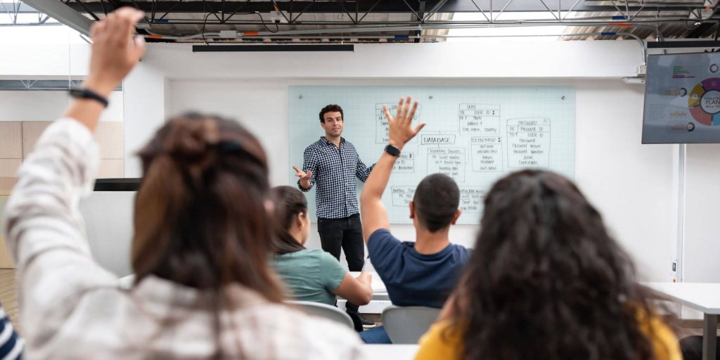 Male professor teaching class, students raising hands